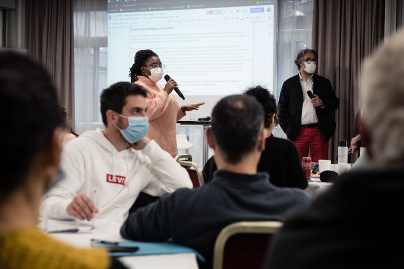 Conférence Citoyenne sur l'aide, l'entraide et les solidarités, 2021 - Une participante prend la parole au micro, les autres l'écoute avec attention