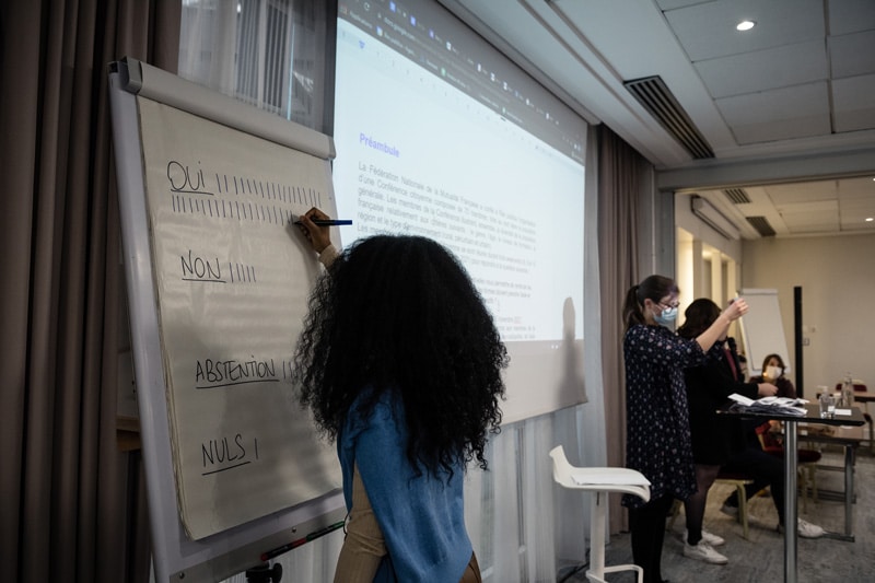 Conférence Citoyenne sur l'aide, l'entraide et les solidarités, 2021 - Une participante prend des notes sur un tableau blanc